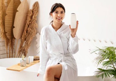 Evdeki modern banyodaki küvette oturan çekici bayan duş jeli ya da şampuan şişesi reklamı yapan güzellik ürünleri kameraya gülümsüyor. Vücut Bakımı Kozmetik Reklamları