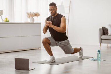 Sportif siyahi adam evdeki online antrenmanı izlerken dizüstü bilgisayarın önünde hücum egzersizi yapıyor. Erkek Fitness Rutini ve Spor Motivasyon Konsepti. Seçici Odaklanma