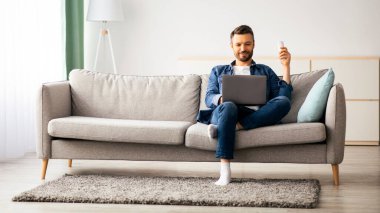 Evde dizüstü bilgisayarı olan, rahat orta yaşlı bir adam, internette sörf yapıyor veya film seyrediyor, AC kumandasıyla el kaldırıyor, kopyalama uzayı kullanıyor. Ev için soğutma sistemleri, klima konsepti