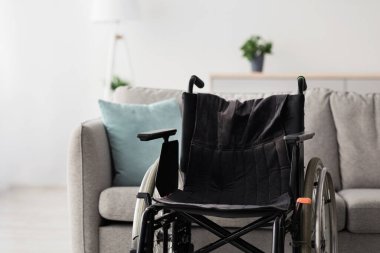 Engelli insanlar için ekipman, yaralanan ve felç olan insanlar için, evde ve klinikte. Siyah, modern, basit tekerlekli sandalye. Oturma odasında içi koltuklu, gri duvarlı arka planda kimse yok.