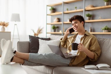 Neşeli Asyalı, serbest çalışan, kahve içen, cep telefonuyla konuşan, iş yerinde bilgisayar başında arkadaşlarıyla konuşan arkadaşlarıyla konuşan, koltukta dinlenen,