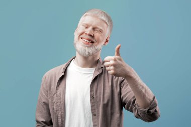 En iyi seçenek. Mutlu albino adam iyi bir şeyi onaylıyor ya da tavsiye ediyor. Adam pozitif jest yapıyor ve gülümsüyor, gri stüdyo arka planında poz veriyor.