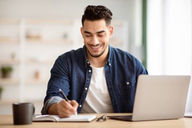 Ofiste dizüstü bilgisayarla çalışırken not alan neşeli Arap adam, sabahları gününü planlayıp, mekanı kopyalıyor. Yeni iş fırsatları arayan, internette sörf yapan mutlu bir orta doğu serbest çalışanı.