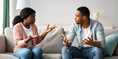 İlişki sorunları ve kriz konsepti. Kızgın siyah adam ve kadın evdeki kanepede oturuyor, kavga ediyorlar, uzayı kopyalıyorlar. Kızgın Afrikalı Amerikalı adam ve kadın birbirlerine bağırıyorlar.