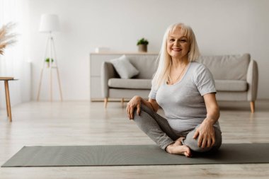 Aktif Yaşam Tarzı Konsepti. Evde kelebek yoga pozu veren çekici, formda bir kadın. Bedava fotokopi alanı. Motive olmuş yaşlı kadın esneklik egzersizleri yapıyor, kameraya bakıyor.