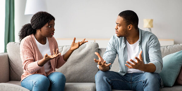 Проблемы отношений и кризисная концепция. Злой черный мужчина и женщина сидят дома на диване, ссорятся, копируют пространство. Разъяренный африканский американец и женщина кричат друг на друга