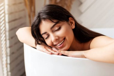 Rahatlatıcı banyo. Evdeki modern banyoda gözleri kapalı bir şekilde banyo yapan mutlu bir kadın. Lüks Spa 'da Bayan Güzellik Ritüeli. Sıhhat ve rahatlama. Panorama, Seçici Odaklanma