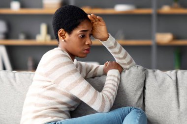 Kötü bir gün. Oturma odasında oturan üzgün Afrikalı Amerikalı bir kadının portresi, depresif siyah bir kadının kafaya dokunması ve bir şeyler düşünmesi, koltukta dinlenmesi, boş bir alan.