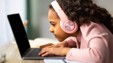 Gençlik ve teknoloji kavramı. Dizüstü bilgisayar kullanan, bilgisayar kullanan, bilgisayar başında oturan siyah bir kız öğrenci. Görme sorunu olan küçük bir kız.