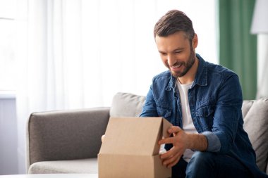 Mutlu orta yaşlı bir adam posta kutusunu açıyor, çay masasının yanındaki kanepede oturuyor, evin içinde. Memnun müşteri, neşeli adam paketi açıyor, internetten kıyafet ya da araç gereç sipariş ediyor, kopyalama alanı