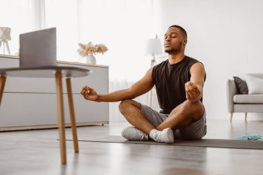 Çevrimiçi yoga. Huzurlu Afrikalı Amerikalı Adam Lotus pozisyonunda oturmuş evde meditasyon videosu izleyerek meditasyon yapıyor. Meditasyon Rahatlatıcı Uygulama ve Egzersiz
