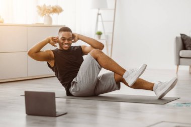Antrenman yapıyorum. Diz dirseğe antrenman yapan mutlu siyahi adam dizüstü bilgisayarda egzersiz yapıyor evde online antrenman izliyor. Spor adam oturma odasında karın kaslarını kasıyor.