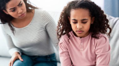 Aile Yanlış Anlaması, Çocukluk Sorunları. Üzgün siyah kız kanepede oturuyor, evde kavga ettikten sonra annesine dönüyor, üzgün kadın kızgın kıza ne olduğunu soruyor.