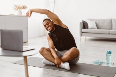 Antrenman yapıyorum. Mutlu sporcu siyahi adam dizüstü bilgisayarda esneyerek evde yerde oturuyor. Sporcu Afrikalı Amerikalı Adam Spor Keyfini Çıkartıyor Rutin Video İzleme Kursu Oturma Odasında