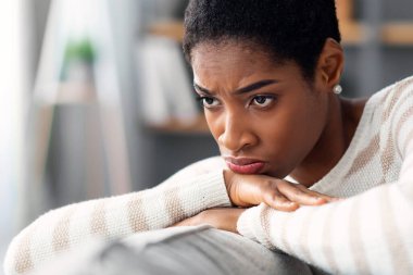 Depresyonu kilitle. Kederli Afro-Amerikan kadın portresi. Evdeki koltukta oturan ve uzaklara bakan düşünceli siyah kadın yalnızlık ve melankoli sırasında acı çekiyor.