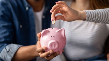 Aile Birikimleri. Çok kültürlü bir çiftin evde otururken domuz kumbarasına madeni para koyarken, eşleri tarafından tanınmayan ve gelecek için para biriktiren çok kültürlü çiftlerin yakın plan fotoğrafları.