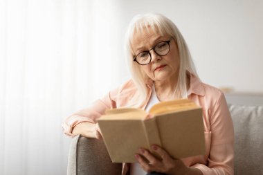 Dinlenme ve gevşeme kavramı. Gözlük takan, elinde kağıt kitap olan, elinde kanepede oturup edebiyat okuyan, hikayeden zevk alan, bedava fotokopi çeken son sınıf öğrencisinin portresi.