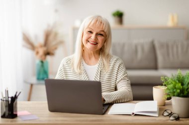Halk ve Teknoloji Konsepti. Mutlu Gülümseyen Kıdemli Bayan Çalışırken veya Laptop Kullanırken, İçişleri Bakanlığı 'nda Masada Otururken, Ücretsiz Kopya Alanı Pozitif Olgun Kadın Kameraya Bakıyor