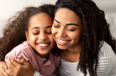 Bağ ve Birliktelik Konsepti. Afrika kökenli Amerikalı anne ve kızın yakın portresi sarılıp gülümsüyor, anneler gününü kutluyor, birlikte vakit geçiriyorlar. Mutlu kadın, kıza sarılıyor.