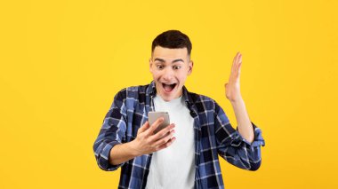 Normal kıyafetli, akıllı telefona bakan heyecanlı bir milenyum adamı. Kazandığı için mutlu ya da turuncu stüdyo geçmişinde başarılı olduğu için. Mobil cihazlı duygusal genç adam online satışa ya da indirime hayret etti