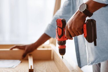 Mobilya tamircisi. Tanımlanamayan siyah adam masayı topluyor, masa detaylarını elektrikli matkapla düzüyor, yakın plan, ekin, kopyalama alanı. Tahta delme işinde tecrübeli genç bir zanaatkar.