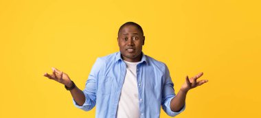 Kafa karışıklığı, şok ve hayal kırıklığı, yüz ifadesi. Şaşırmış üzgün Afro-Amerikan yakışıklı adam kollarını yana açıyor, turuncu arka planda izole edilmiş, stüdyo çekimi, boş alan.