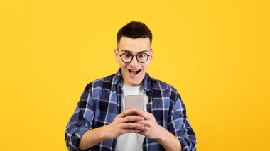 Çevrimiçi iletişim, iş ya da turuncu stüdyo geçmişi için cep telefonu kullanan genç bir adam. Mobil cihazlı havalı adam online videolar izliyor, web 'i arıyor.