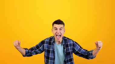 Heyecandan çığlık atan mutlu milenyum çocuğu, iki eli turuncu stüdyo geçmişinde EVET işareti yapıyor. Gayri resmi giyinmiş muzaffer genç adam, başarısını kutluyor.