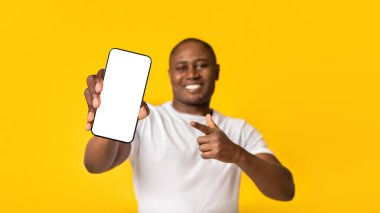 Harika bir uygulama, online teklif ve popüler blogcudan tavsiye. Beyaz tişörtlü, gülümseyen Afro-Amerikan adam, sarı arka planda izole edilmiş, boş ekranlı parmağını telefonda gösteriyor.