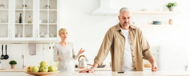 Öfkeli eş kocasını suçluyor, evde evlilik sorunları var. Covid-19 salgını ve kötü ilişkiler. Alınan yetişkin beyaz erkek mutfak içinde küfreden kızgın dişiyi dinliyor, panorama.