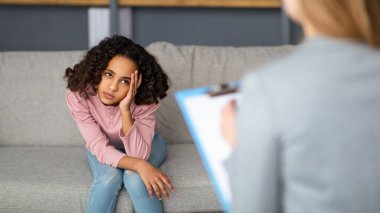 Kadın çocuk psikoloğu ofiste ya da evde siyahi bir kızla çalışıyor. Üzgün bir genç hasta terapi seansında duygularından bahsediyor.