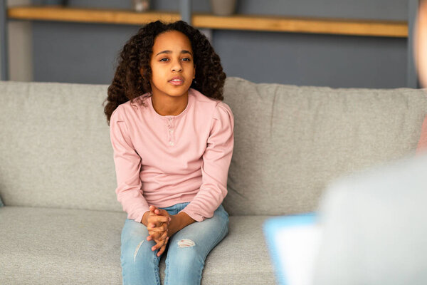 Psychologist working with upset african american girl in office, sad teenager patient talking about her feelings, problems and trauma to psychotherapist, sitting on couch