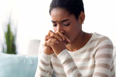 Umutsuzluk Konsepti. Depresyonda olan Afro-Amerikan kadın portresi, elleri kanepede bağlı oturan, gözleri kapalı üzgün, ruhsal sinir krizi geçiren siyah kadın.