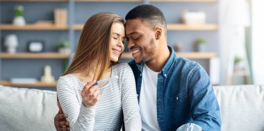 Ebeveyn Olmak Konsepti. Romantik Çok Irklı Eşler Pozitif Hamilelik Testi Tutarken Koltukta Birlikte Rahatlarken Mutlu Irklar Arası Çiftler Kucaklaşır ve Dokunur Alınır