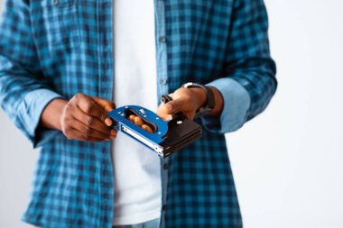 Tanımlanamayan siyah marangoz elinde inşaat zımbası, evde çalışmaya ve mobilyaları onarmaya hazır, beyaz arka planda duruyor.