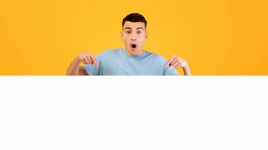 Kafkasyalı bir adamın portresi turuncu stüdyo arka planındaki boşluğu işaret ediyor. Şaşırmış genç bir adam reklam yapıyor, büyük indirim ya da indirim yapıyor.