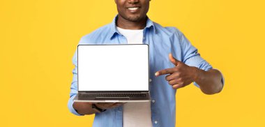 Mükemmel bir internet uygulaması, iyi bir site, online satış ve blog yazarı tavsiyesi. Gülümseyen orta yaşlı Afro-Amerikalı adam dizüstü bilgisayarı boş gösteriyor, sarı arka planda izole edilmiş, stüdyo çekimi, kesilmiş.