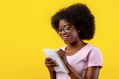 Gözlüklü zeki Afro-Amerikan bayan öğrenci. Kontrol listesi yazıyor. Telif defterine not alıyor.