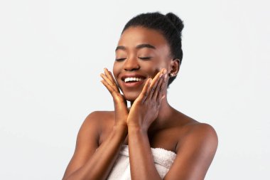 Doğal konsept. Çekici Afrikalı Amerikalı kadın yumuşak, pürüzsüz tenine dokunuyor, güzellik tedavisinin tadını çıkarıyor, gri arka planda duruyor.