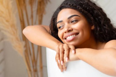 Mutlu Afrika kökenli Amerikalı kadın evdeki modern banyoda küvette uzanarak rahatlatıcı bir banyo yapıyor. Bayan Banyo Bakışları, Lüks Spa 'da Güzellik Ritüeli. Rahatlama ve sağIık. Panorama