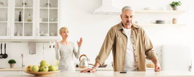 Çiftler evlerinde mutfaklarında anlaşmazlıklar, aile içi kavgalar ve ilişkilerde sorunlar yaşarlar. Sinirli orta yaşlı kadın gücenmiş kocaya bağırıyor modern mutfak, panorama, fotokopi odası