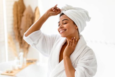 Sağlık ve Spa. Modern banyoda ayakta duran, beyaz bornozla dans eden, duştan sonra güzellik rutininin tadını çıkaran mutlu Afrikalı Amerikalı kadın. Vücut Bakımı ve Hijyen Konsepti
