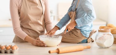 Tatlı küçük siyah kız ve genç anne cam kaseye hamur karıştırıyorlar çırpıcı kullanarak, kızı mutfakta yemek masasında oturuyor. Aile ev yapımı hamur işleri yapmaktan, yemek yapmaktan ve evde eğlenmekten hoşlanıyor.