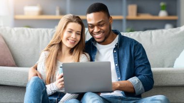 Mutlu, genç, çok kültürlü bir çift evde dizüstü bilgisayarla rahatlıyor, neşeli siyah adam ve beyaz kadın oturma odasında otururken internetten film izliyor ya da alışveriş yapıyorlar.