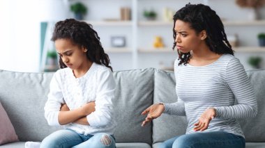 Kızgın Afrikalı Amerikalı anne, üzgün kızını azarlıyor kollarını göğüslerine kavuşturup, evde birlikte kanepede oturuyor, fotokopi çekiyor. Siyah anne ve çocuk kavga ediyor, oturma odası içinde.