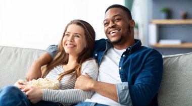 Ev randevusu. Neşeli ırklar arası çift koltukta dinleniyor, TV seyrediyor ve patlamış mısır yiyor, mutlu siyah adam ve beyaz kadın sıcak oturma odasında dinleniyor, ev eğlencelerinin keyfini çıkarıyor,