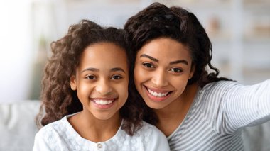 Neşeli siyah anne ve kızı evde birlikte eğlenirken selfie çekiyorlar, yakın plan portre. Mutlu Afrikalı Amerikalı genç kadın güzel kızıyla vakit geçiriyor, fotoğraf çekiyor.