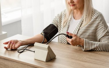 Sağlık ve Hipertansiyon problemi. Yaşlı kadın evde otururken atardamar basıncını ölçüyor. Yüksek Tansiyon Konsepti. Seçici Odaklanma, Yan Görünüm, Yakın Çekim