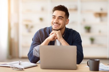 Keyifli bir Arap serbest çalışanı evden bilgisayarla çalışırken fotokopi odasına bakar çalışma masasında oturur ve ellerini uzatır. Çevrimiçi iş fırsatları, ev kavramından çalışmak