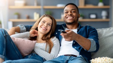 Yurtiçi Hobi. Patlamış mısırlı mutlu bir çift evde televizyon izliyor, ırklar arası eşleri seviyor oturma odasında rahat bir koltukta dinleniyor, uzaktan kumandayla kanal değiştiriyor.